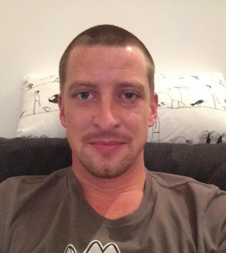 Ein Mann mit einem freundlichen Gesichtsausdruck sitzt auf einer Couch.