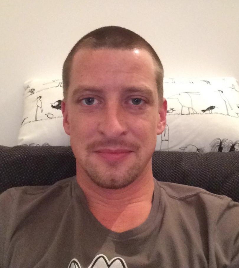 Ein Mann mit einem freundlichen Gesichtsausdruck sitzt auf einer Couch.