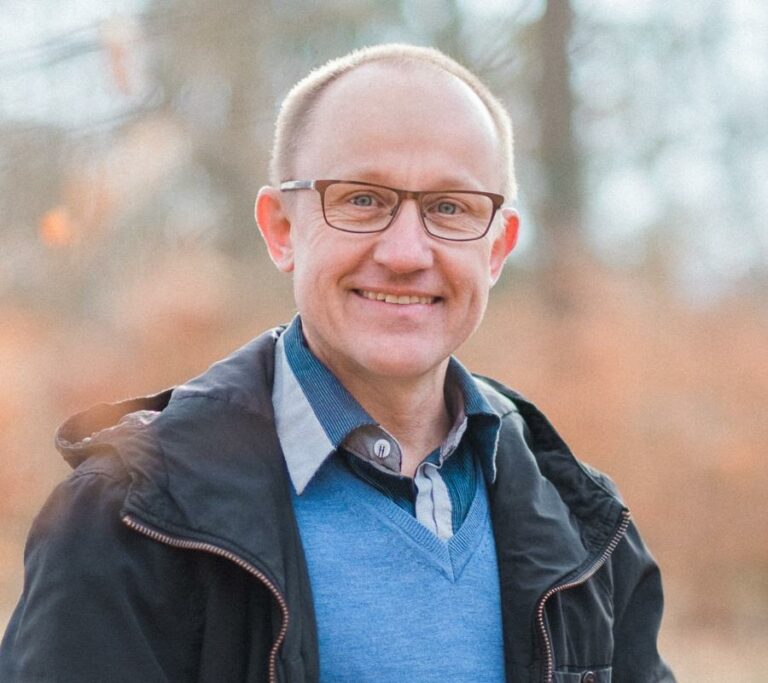 Ein Mann mit Brille und freundlichem Lächeln im Freien