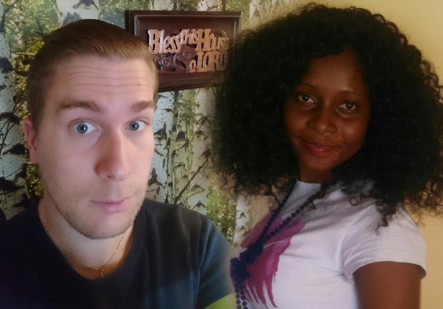 Ein Mann und eine Frau stehen nebeneinander und lächeln in die Kamera. Im Hintergrund ist ein Schild mit der Aufschrift 'Bless This Home' zu sehen.