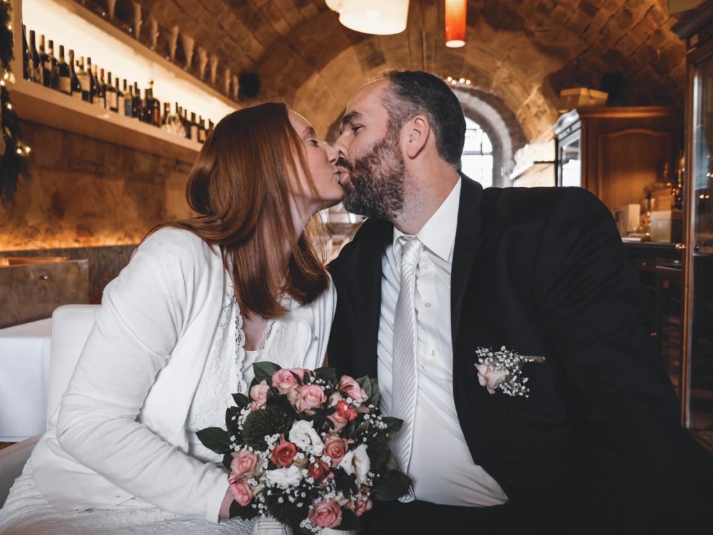 Ein Brautpaar küsst sich im Restaurant, die Braut hält einen Blumenstrauß.