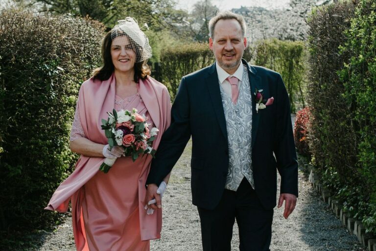 Eine elegant gekleidete Frau mit Blumenstrauß und ein Mann in Anzug gehen nebeneinander.