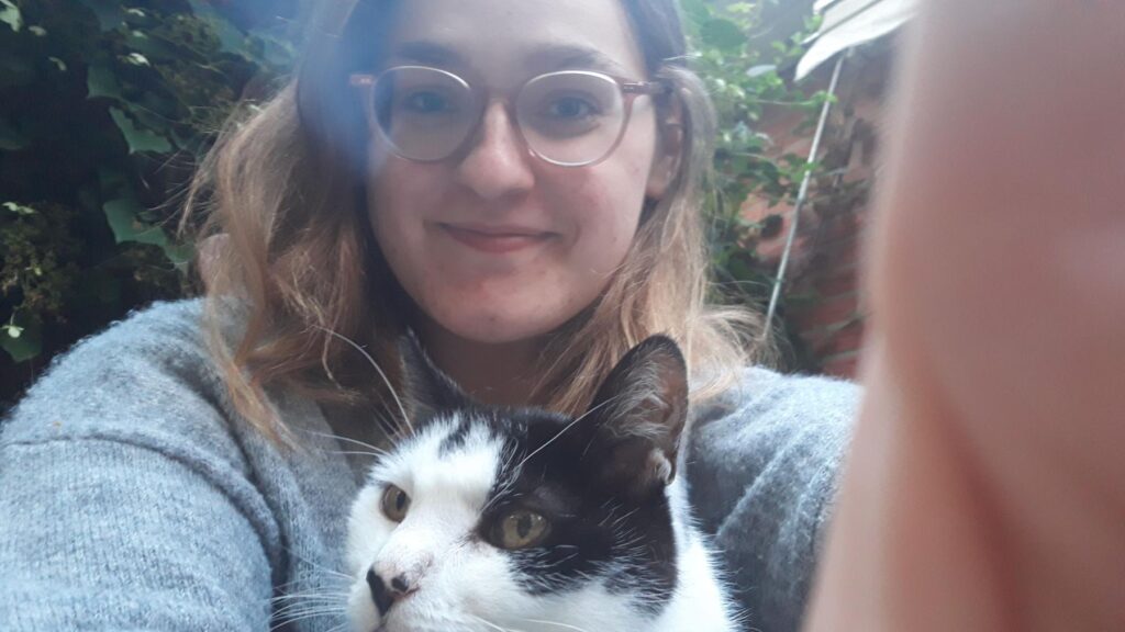 Ein Mädchen mit langen Haaren und Brille hält eine schwarze und weiße Katze im Arm. Die Katze schaut nach links.