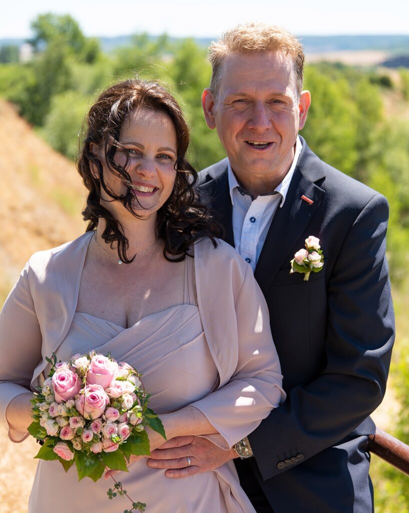Ein Paar in Hochzeitskleidung, die Frau hält Blumen in der Hand.
