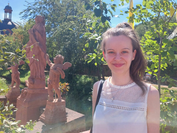 Eine junge Frau in weißem Kleid steht neben Statuen